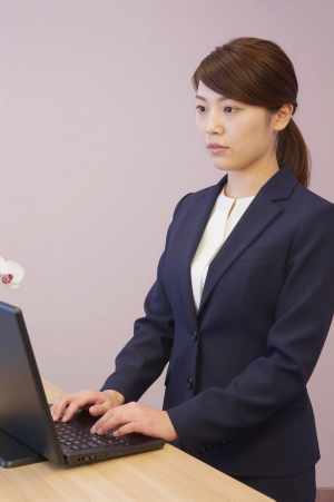 ホテル受付でPC作業と来客対応する女性