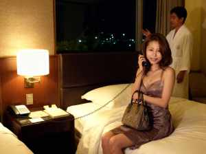 夜のホテルの部屋のベッドに座り、笑顔で電話で話す女性。