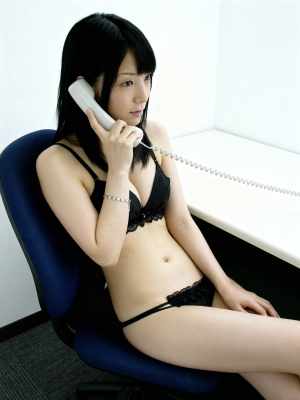 黒いレースのブラジャーとそれに合うパンティーを着て、机に座って電話で話している若い女...。