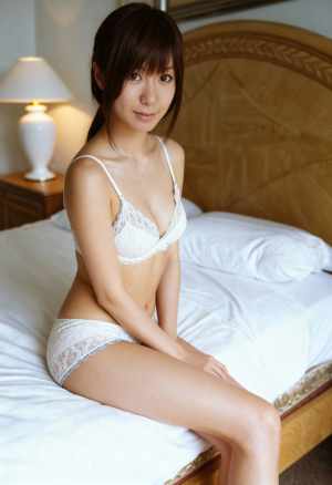 居心地の良い寝室でベッドに座り、白いレースのブラジャーとそれに合ったパンティーを身に...。