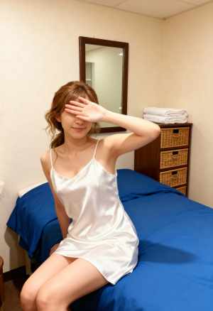 シンプルな寝室の環境でベッドに座り、手で目を覆っている若い女性を正面から写実的に撮影...。