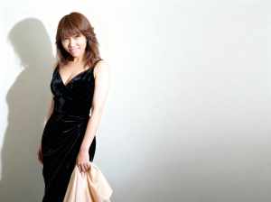 黒のベルベットのフォーマルなドレスを着て、真っ白な壁に立ち、左手にベージュの布を持っ...。