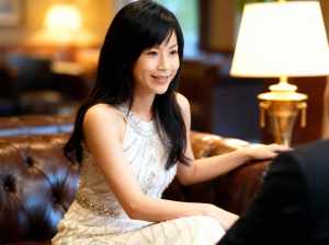 豪華なホテルのロビーで茶色の革張りのソファに座り、白いビーズのドレスを着た若い女性。
