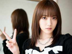 茶色の長いストレートの髪と前髪を持ち、白いリボンが付いた黒いセーターを着て、銀のチェ...。