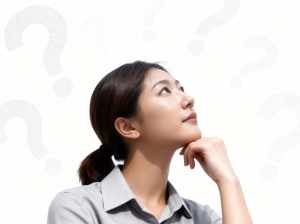 無地の白い背景に疑問符で囲まれた、思慮深い表情をしたアジア系の若い女性を横顔カメラの...。