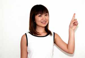 無地の白い背景の前に立つ、陽気な表情の若いアジア人女性。