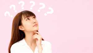 長い茶色の髪と前髪を持ち、白いブラウスを着た若い女性が画像の中央に位置し、無地のピン...。