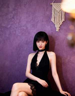 レースのディテールが施された黒いドレスを着て、紫の壁に向かって座っている若い女性を横...。