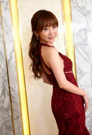 赤いレースのドレスを着た美しいアジア人女性が、金色の縞模様の大理石の壁の前に立ち、自...。