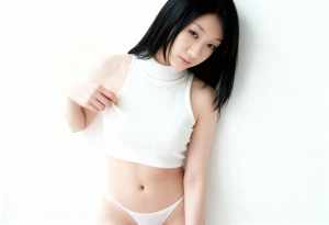 白いリブ編みのノースリーブトップスとそれに合ったパンティーを着て、無地の白い壁に向か...。