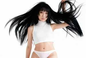 白いリブ編みのクロップトップとそれと一致するパンティーを着て、長い黒髪でポーズをとる...。