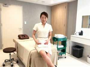 スパの設定でマッサージ テーブルに座り、カメラに向かって微笑む女性をフロント カメラ...。