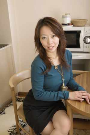 青いセーターと黒いスカートを着て、居心地の良いキッチンのテーブルに座っている若い女性...。
