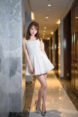 モダンな廊下の大理石の壁に立っている白いドレスを着た若い女性を横から撮影した写実的な写真。