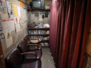 薄暗い部屋の右側に赤いカーテンがあり、壁にはポスターが貼られています。