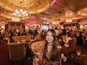 高級レストランに座ってコニャックのグラスを持ち、カメラに向かって微笑む女性を正面カメ...。