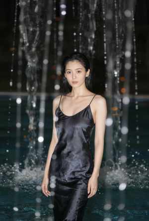絹のような黒いスリップ ドレスを着て、夜の噴水の前に立つ若い女性を正面カメラ アング...。