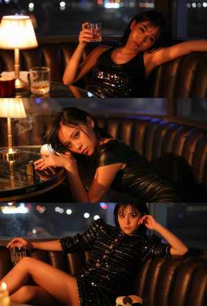 背景にぼやけた夜の街並みを背景に、黒いスパンコールのドレスを着た若い女性が革張りのソ...。