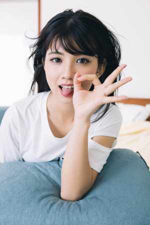 屋内で青いクッションに横たわり、遊び心のある表情でふざけてポーズをとる若い女性を、ク...。