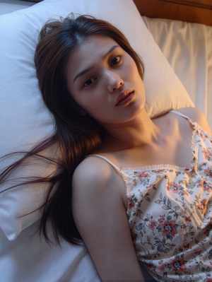 ベッドに横たわり、瞑想的な表情でカメラをまっすぐ見つめている若い女性をクローズアップ...。