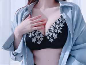 水色のボタンアップシャツと白い花柄の刺繍が入った黒いブラジャーを着た、茶色の長い髪の...。