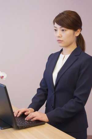 ホテル受付でPC作業と来客対応する女性