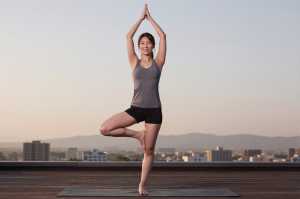 屋上でヨガの木のポーズをとる男性