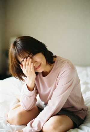 ピンクのセーターとグレーの短いスカートを着て、柔らかい表情でベッドに座る若い女性を正...。