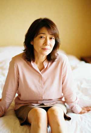 柔らかく暖かい光の中でベッドに座る中年のアジア人女性のポートレート。