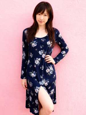 サイドにスリットの入ったネイビーブルーの花柄のドレスを着て、ピンクの壁に立っている若...。