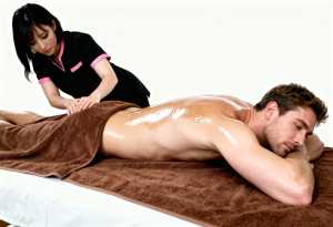 黒とピンクの制服を着た女性を伴い、茶色のタオルで覆われたマッサージ台に横たわる男性を...。