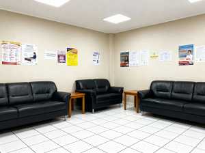 部屋の中央に 3 つの黒い革張りのソファと 2 つの小さな木製テーブルがある待合室の...。