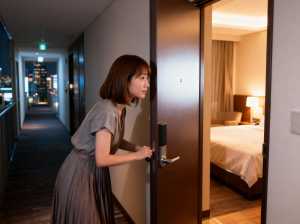 背景の窓から見える街のスカイラインを背景に、夜にホテルの部屋のドアを開ける若い女性を...。