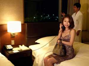 夜のホテルの部屋のベッドに座り、笑顔で電話で話す女性。