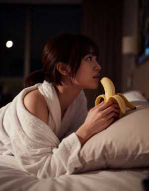 白いバスローブを着た若い女性がバナナを手にベッドに横たわっている様子を横から撮影した...。