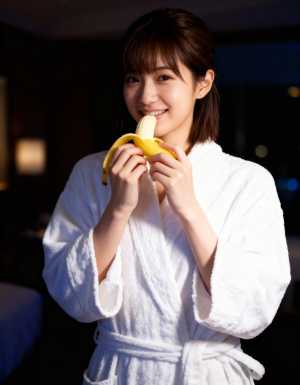 白いバスローブを着た若い女性が顔の前にバナナを持ち、満面の笑みを浮かべている、正面カ...。