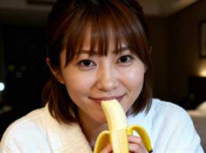 白いローブを着て、皮をむいたバナナを顔の前に持つ、短い茶色の髪の若い日本人女性の接写。