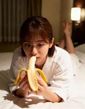 ホテルの部屋のベッドに横たわり、皮をむいたバナナを顔の前に持っている若い女性。
