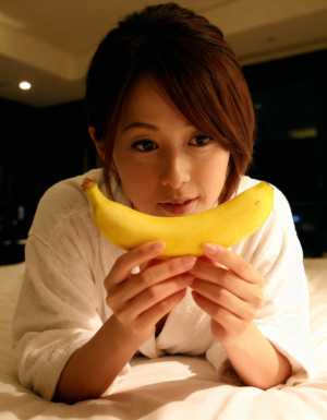 ベッドに横たわり、顔の前にバナナを持った若い女性。