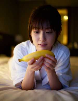 薄暗い寝室のベッドに横たわり、顔の前にバナナを持った若い女性をクローズアップ カメラ...。