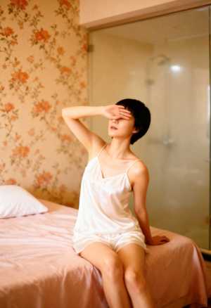 右手で目を覆い、瞑想的な表情でベッドに座っている若い女性を横から撮影した写実的な写真。