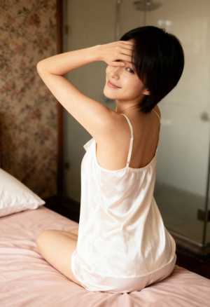 白いシルクのキャミソールとそれに合わせたショートパンツを着て、ベッドに座り、お茶目な...。