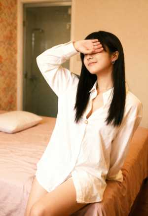 ホテルの部屋のベッドに座り、右手で敬礼する若い女性。