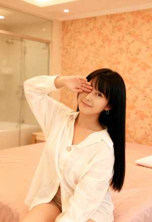 白いボタンダウンのシャツを着て、右手で敬礼しながらベッドに座っている若い女性を横から...。