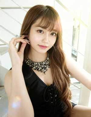 ウェーブのかかった茶色の長い髪と前髪を持ち、主張のあるネックレスが付いた黒いドレスを...。