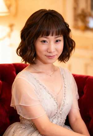 柔らかく温かみのある照明が照らされた豪華な部屋で、赤いベルベットのソファに座っている...。