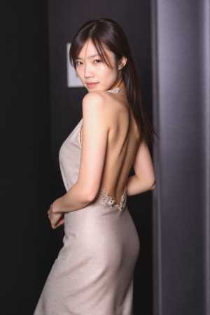 背中の開いたデザインのフォーマルドレスを着た女性が、暗い壁と柱のある薄暗い部屋に立つ...。