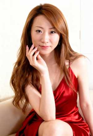 赤いサテンのドレスを着て、リラックスしたポーズでベージュのソファに座る、長くウェーブ...。