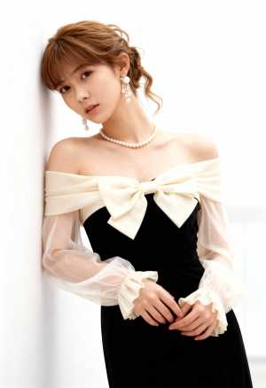 薄手の袖と大きなリボンが付いたフォーマル ドレスを着て、真っ白な壁に向かってポーズを...。