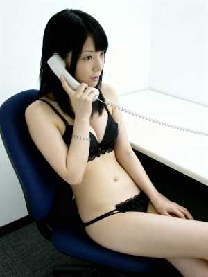 黒いレースのブラジャーとそれに合うパンティーを着て、机に座って電話で話している若い女...。